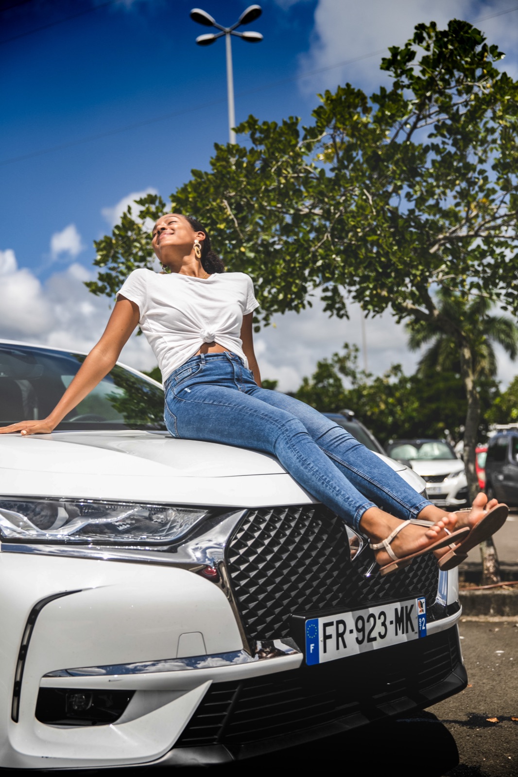 Jeune femme heureuse sur le capot d'une DS3 Crossback E-Tense électrique en Outre-mer